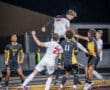 High school soccer players leap for the ball in a competitive match under the stadium lights, showcasing athleticism.