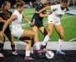High school girls' soccer match action, featuring intense play as players compete for the ball on the field at night.