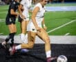 High school soccer players in action during a game, focusing on a player dribbling the ball down the field.