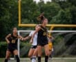 Girls' soccer players compete fiercely as the ball soars overhead on a vibrant field during a game.
