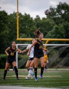 Two female soccer players compete for the ball during an intense match on a grassy field, showcasing athleticism and teamwork.