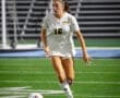 A soccer player in a white uniform with number 16 runs towards the ball on a well-lit turf field.