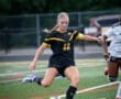Female soccer player in black uniform dribbling a ball on the field during a match, showcasing athletic skill.