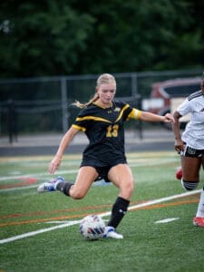 Female soccer player in black uniform dribbling a ball on the field during a match, showcasing athletic skill.