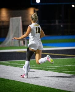Soccer player in white jersey with Tigers and number 19 runs on the field at night, preparing to kick the ball.