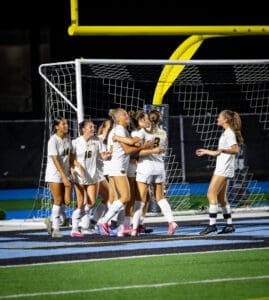 Soccer team celebrating a goal under stadium lights, showcasing teamwork and excitement on the field.
