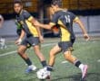 Two young soccer players in black and yellow jerseys engage in a game on a nighttime field, focusing on the ball.