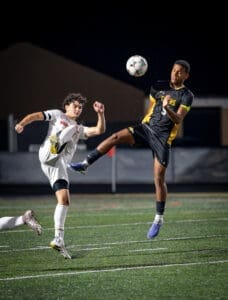 Two soccer players compete for the ball during a night game, showcasing athleticism and dynamic movements on the field.