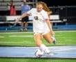 A soccer player in a white jersey kicks a ball on a field during a night game. Focused and determined.
