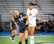 Two female soccer players compete for the ball in mid-air during a night game, showcasing athleticism and determination.