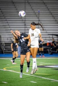 Two female soccer players compete for the ball in mid-air during a night game, showcasing athleticism and determination.