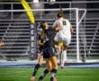 Two female soccer players compete for a high ball during a night game on a well-lit field.