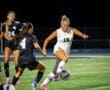 Female soccer players in action during a night game, one dribbling the ball, showcasing athleticism and competition.
