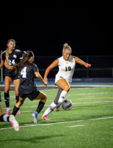 Female soccer players in action during a night game, one dribbling the ball, showcasing athleticism and competition.