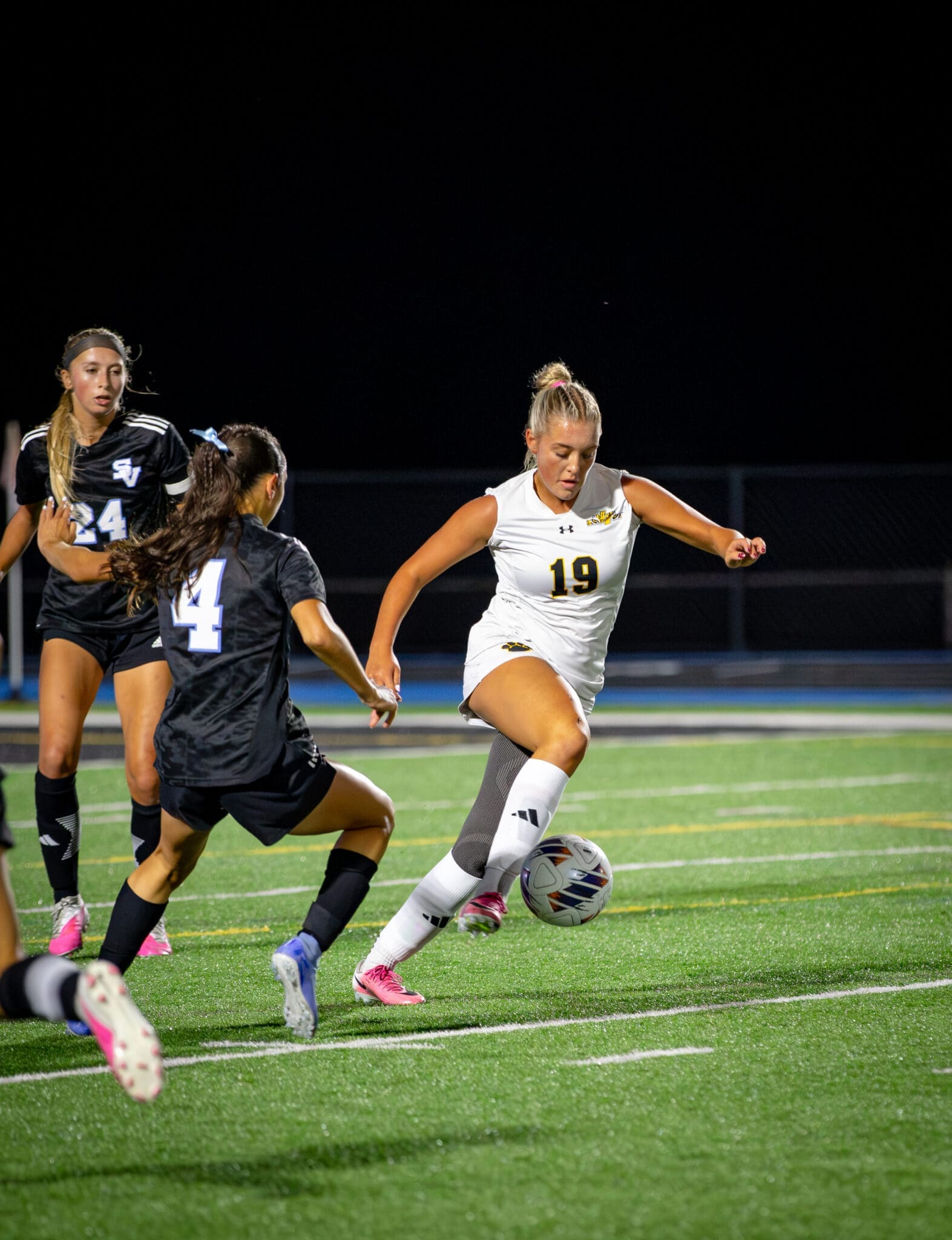 Female soccer players in action during a night game, one dribbling the ball, showcasing athleticism and competition.