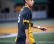 Young soccer player in black and yellow uniform, walking on a field during a night game, focused and determined.