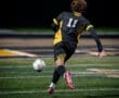 Young soccer player wearing jersey number 11 kicks a ball on a brightly lit field during a night game.