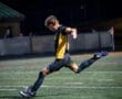 Youth soccer player in action, kicking the ball on a illuminated field during a dynamic night game.