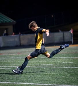 Youth soccer player in action, kicking the ball on a illuminated field during a dynamic night game.