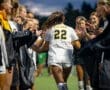 Team members cheer as player #22 of the Tigers runs through a victory tunnel during a soccer game.