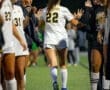 North Allegheny soccer player #22 receives high fives from teammates after a match on a field under a dusky sky.