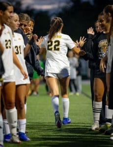 North Allegheny soccer player #22 receives high fives from teammates after a match on a field under a dusky sky.