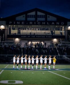 Pine-Richland soccer team standing in line during national anthem at night, with fans in the background at the stadium.
