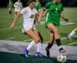 Two female soccer players compete for the ball on a well-lit field during a night game.