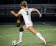 Female soccer player in action during a night game, sprinting towards the ball on a well-lit field.