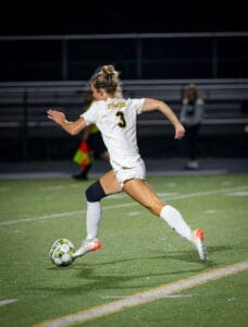 Female soccer player in action during a night game, sprinting towards the ball on a well-lit field.