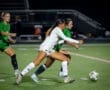 Two female soccer players compete for possession of the ball under stadium lights during a night game.