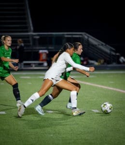 Two female soccer players compete for possession of the ball under stadium lights during a night game.