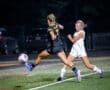 Two soccer players compete for the ball on a field at night, capturing intense action in a competitive match.