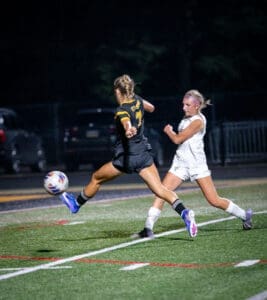 Two soccer players compete for the ball on a field at night, capturing intense action in a competitive match.