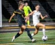 Two female soccer players compete for the ball under stadium lights during a night game, showcasing athleticism and teamwork.