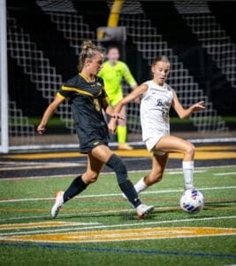 Two female soccer players compete for the ball under stadium lights during a night game, showcasing athleticism and teamwork.