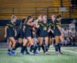 Girls' soccer team celebrating a goal under the night lights on the field, showcasing teamwork and excitement.