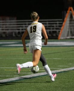 Soccer player in white uniform dribbling a ball on the field at night, focused on the game.