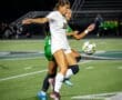 Two female soccer players compete for the ball on a night field, showcasing athleticism during a match.