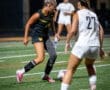 A soccer player dribbles the ball on a field during a night game, showcasing athletic skills and competitive spirit.