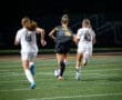 Youth soccer players sprinting across a field at night, aiming for the ball during an exciting match.