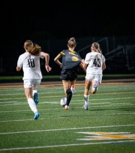 Youth soccer players sprinting across a field at night, aiming for the ball during an exciting match.