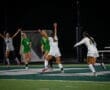 Soccer players celebrate a goal under stadium lights, showcasing excitement and teamwork on the field at night.