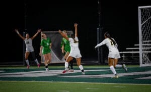 Soccer players celebrate a goal under stadium lights, showcasing excitement and teamwork on the field at night.