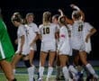 Girls' soccer team celebrating a goal under the night lights on the field, showcasing teamwork and excitement.