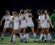 Teams celebrate a goal under the night lights during a high school girls' soccer match. Unity and joy in sports.