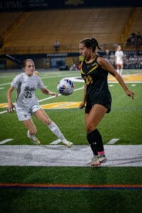 Two female soccer players in a dynamic moment on the field, one dribbling a ball while the other defends actively.