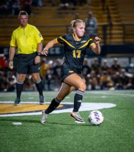 Soccer player wearing jersey number 17 dribbles the ball during night match, with referee in the background.