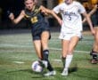 Two female soccer players compete for the ball during a night match, showcasing athleticism and determination on the field.