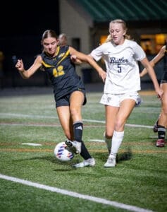 Two female soccer players compete for the ball during a night match, showcasing athleticism and determination on the field.